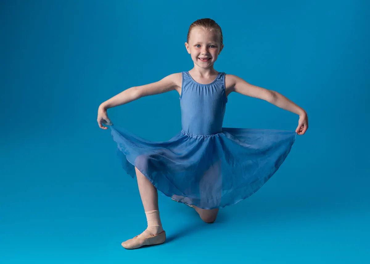 A young dancer in a blue dress against a blue backdrop